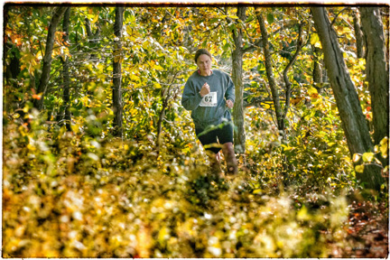A photograph of a marathon contestant running on a forested trail