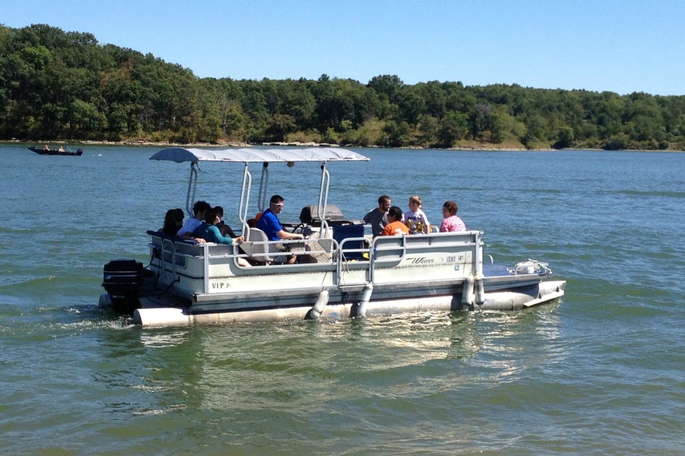 A photograph of lake-goers on a pontoon boat, enjoying a summer day
