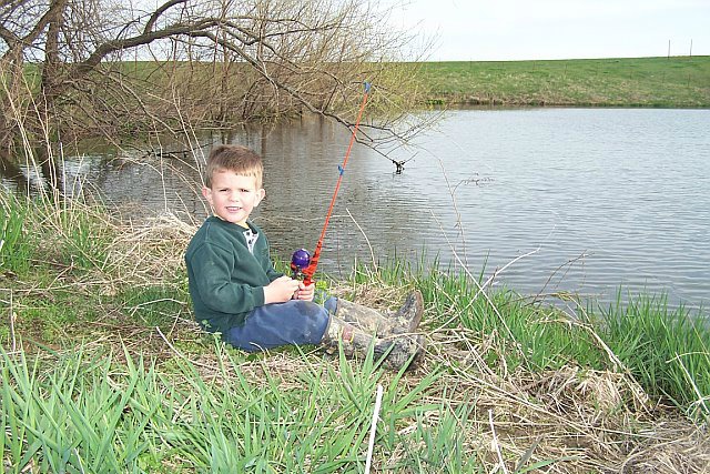 A child with their fishing rod sitting on the shoreline, smiling