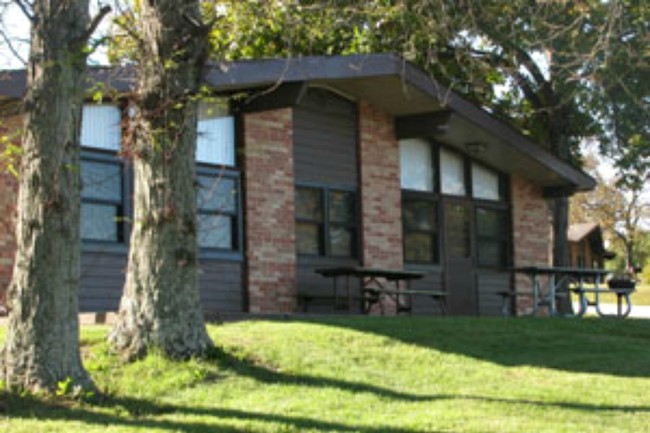 Photograph of the exterior of a cabin at thousand hills state park, showing off the brick and wood construction and a couple picnic tables in front